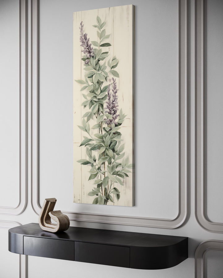Vertical framed canvas wall art featuring sage green basil leaves and purple flowers on a wall.