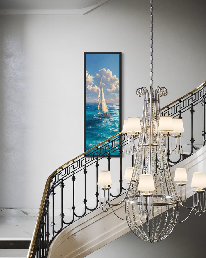 Tall narrow vertical canvas print of a sailboat on a blue ocean in a black frame on a white wall.