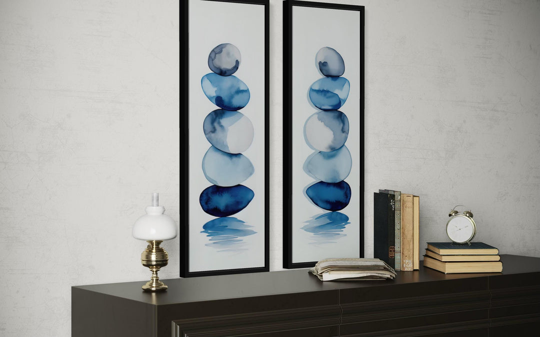 Set of two tall narrow canvas prints featuring blue watercolor stacked zen stones on a white wall.
