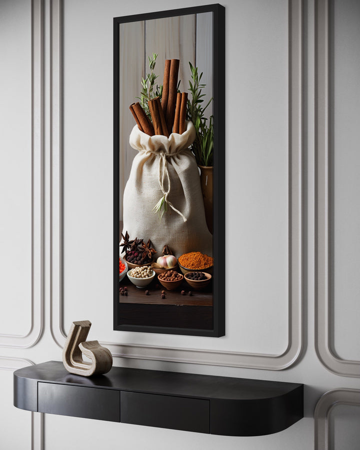 Tall narrow framed canvas wall art of herbs and spices in a kitchen setting above a black console.