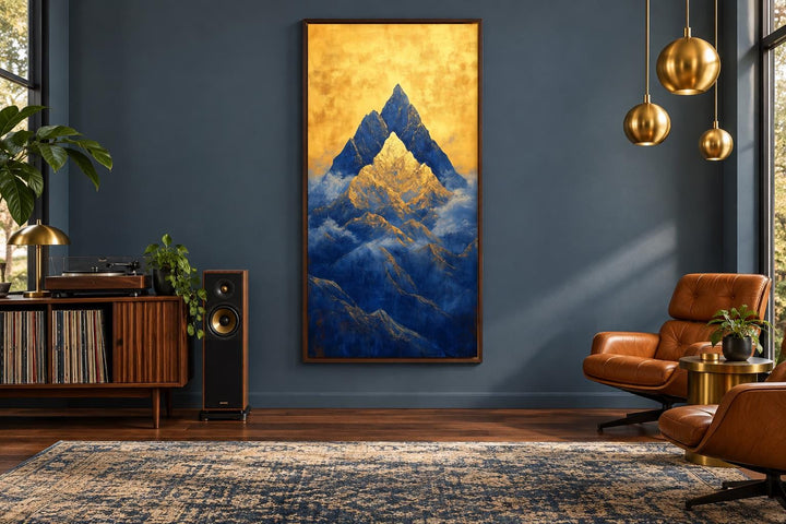 Tall vertical framed canvas wall art of blue mountains under a glowing gold sky in a modern room.
