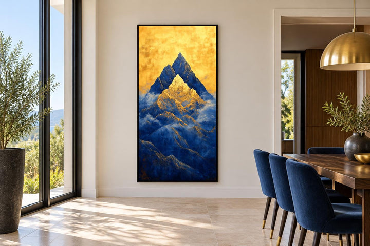 Tall vertical framed canvas wall art of blue mountains under a glowing golden sky in a dining room.