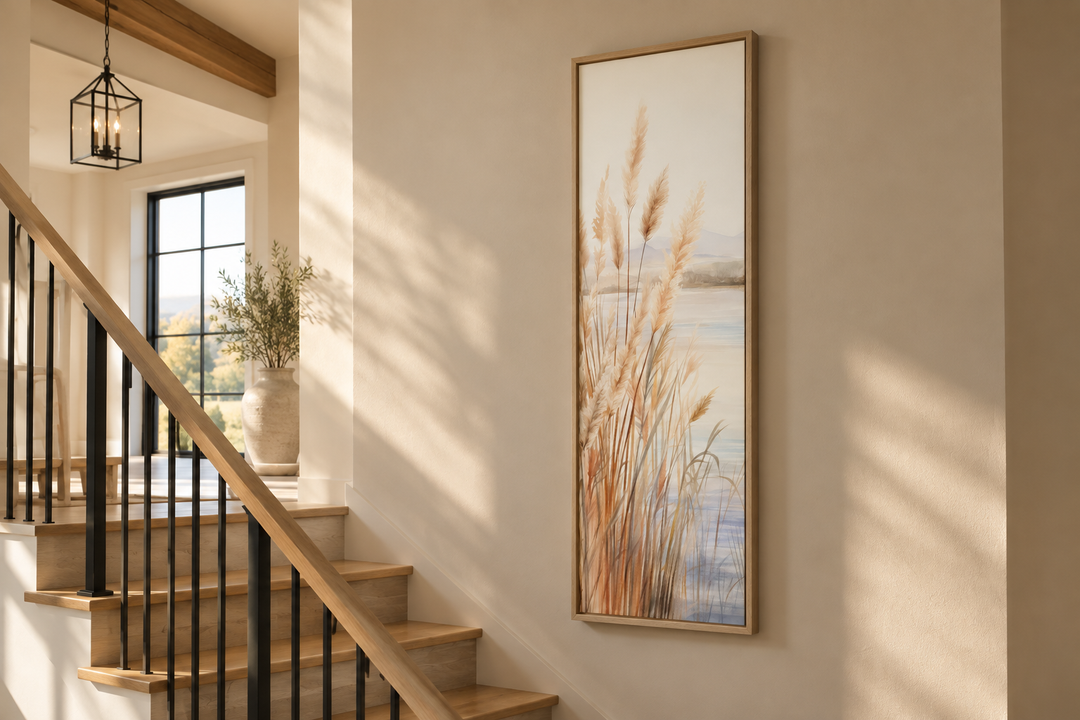 Vertical framed canvas wall art of pampas grass on a beach, hung on a neutral wall near a staircase.