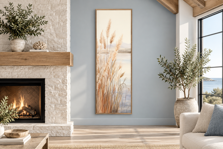 Vertical framed canvas wall art of pampas grass on a beach in neutral tones on a blue wall.