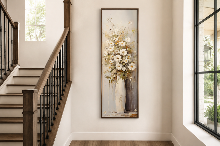 Tall narrow framed canvas art of white wildflowers in a vase on a neutral farmhouse wall.