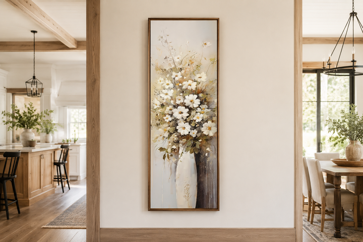 Tall narrow framed canvas wall art of white wildflowers in a vase, hanging in a farmhouse interior.