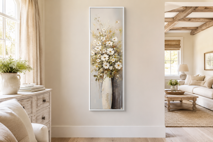 Tall narrow vertical framed canvas wall art of white wildflowers in a vase in a farmhouse room.