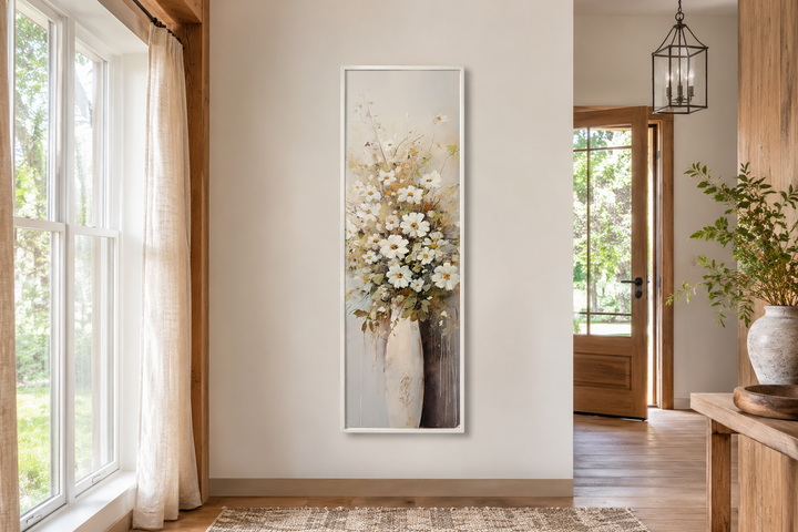 Tall narrow framed canvas wall art of white wildflowers in a vase on a neutral farmhouse wall.