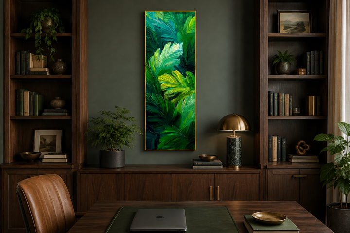 Vertical canvas print of lush green tropical leaves in a tall, narrow gold frame on a dark wall.