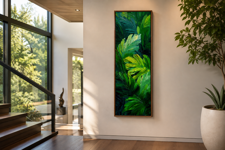 Vertical canvas print of tropical green leaves in a narrow wood frame on a modern white wall.