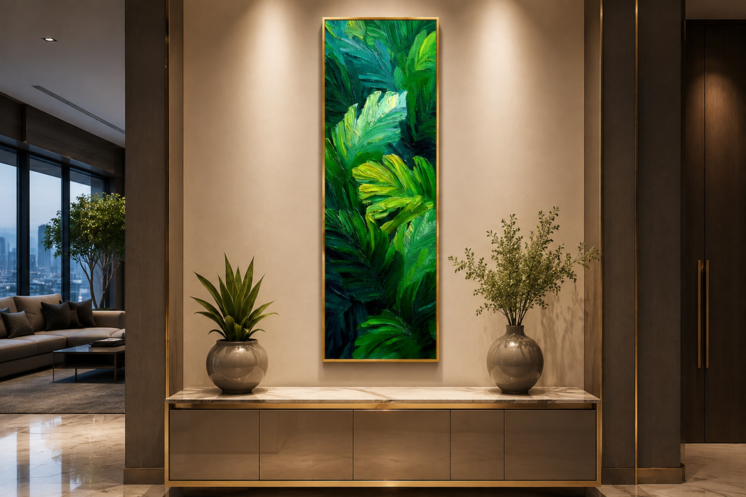 Vertical canvas print of tropical green leaves in a painterly style, framed in gold on a beige wall.
