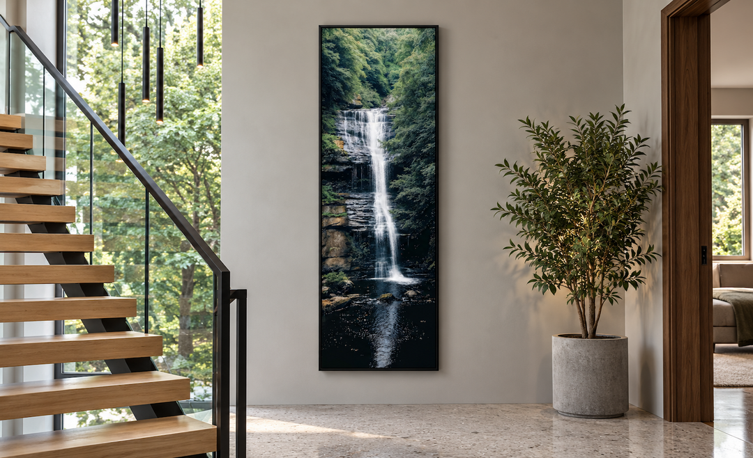Tall narrow vertical framed canvas wall art of a waterfall in a lush forest on a neutral wall.