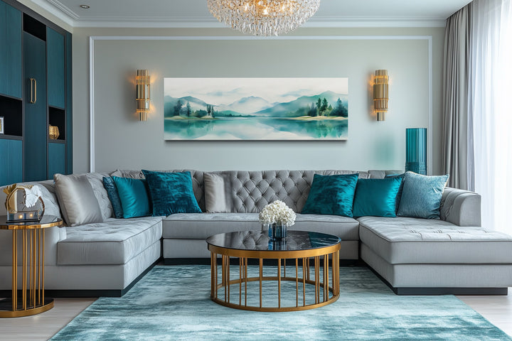 Teal watercolor mountains and lake landscape panoramic wall art above a grey sectional sofa.