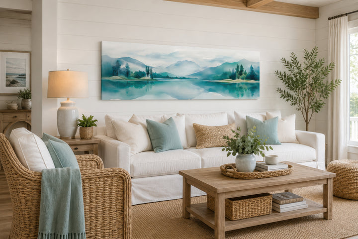 Teal watercolor mountain and lake landscape panoramic wall art hanging above a white sofa.