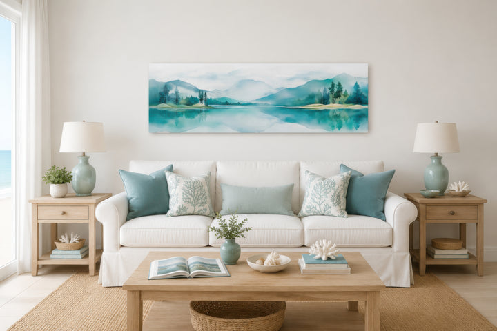 Teal watercolor mountain and lake landscape panoramic wall art hanging above a white sofa.
