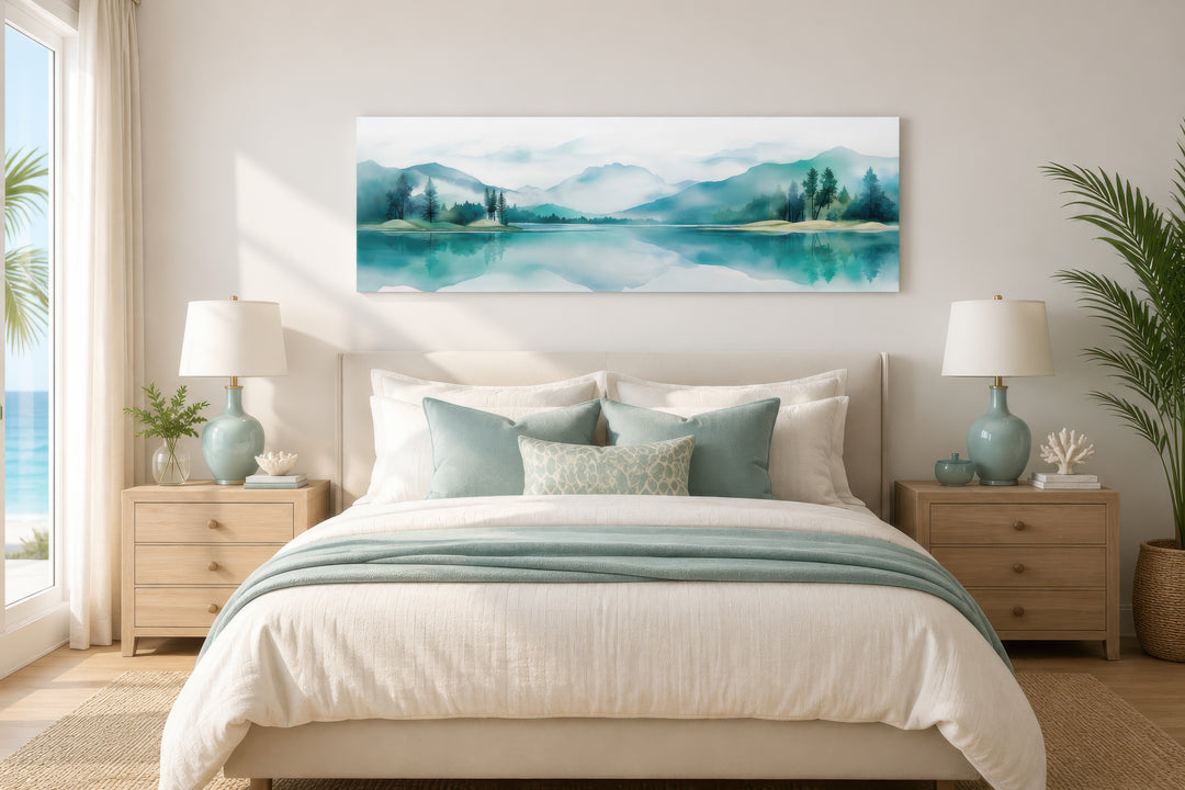 Teal watercolor mountains and lake landscape long narrow canvas art displayed over a bed.