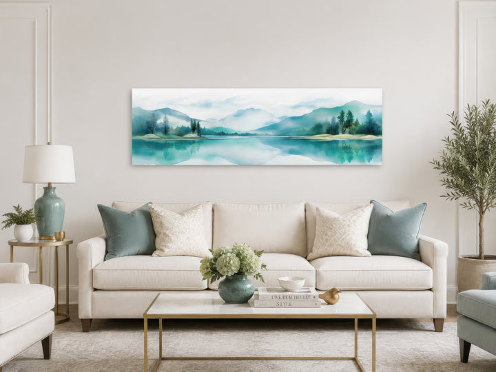 Teal watercolor panoramic wall art of mountains and a lake hanging above a cream sofa.