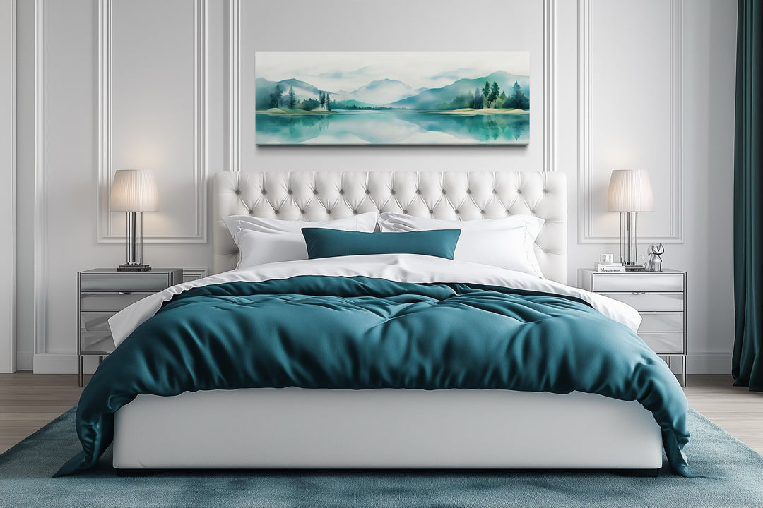 Teal watercolor mountain and lake landscape canvas art displayed above a white tufted bed.