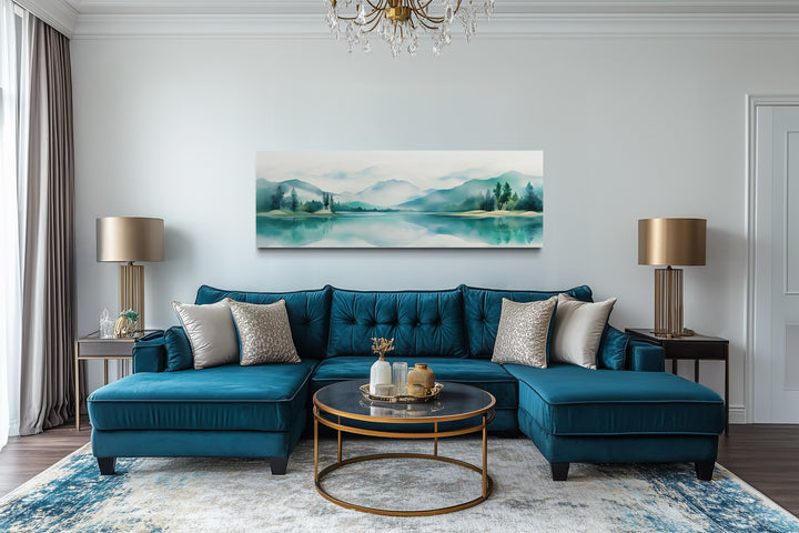 Teal watercolor mountain and lake landscape panoramic wall art displayed above a blue sofa.