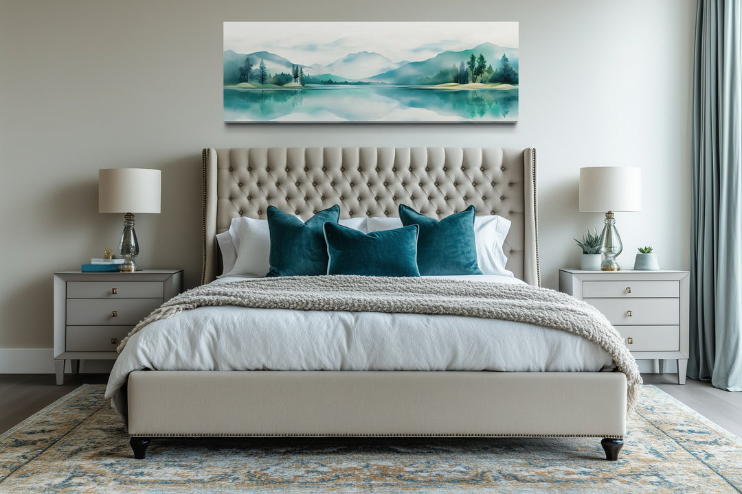 Teal watercolor mountain and lake landscape wall art in a long narrow format above a bed.