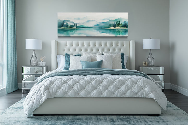 Teal watercolor mountain and lake landscape panoramic wall art hanging above a bed.