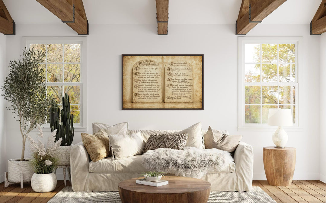 A framed Ten Commandments canvas wall art hangs above a neutral sofa in a bright, rustic living room.