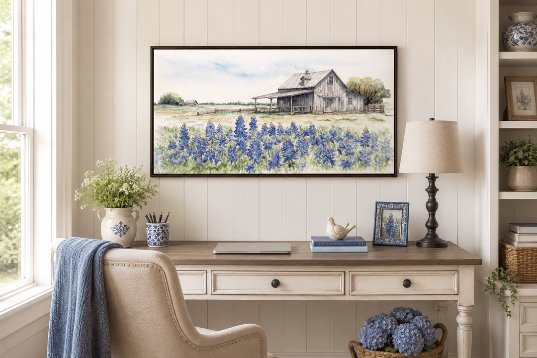 Rustic Texas barn watercolor painting with bluebonnet field in a dark frame above a desk.