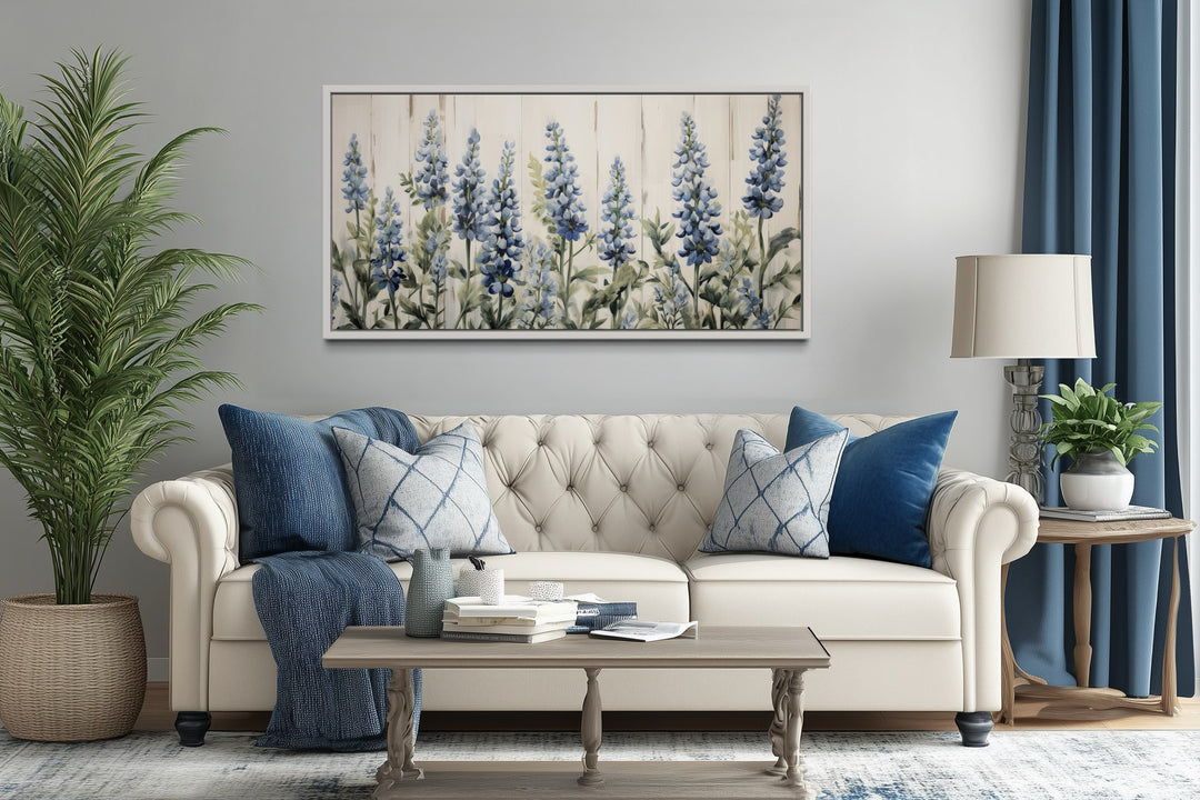 Texas bluebonnets painted on wood rustic framed canvas wall art hanging above a white tufted couch.