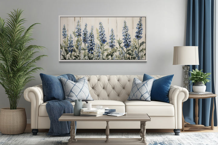 Texas bluebonnets painted on wood rustic framed canvas wall art hanging above a white tufted couch.