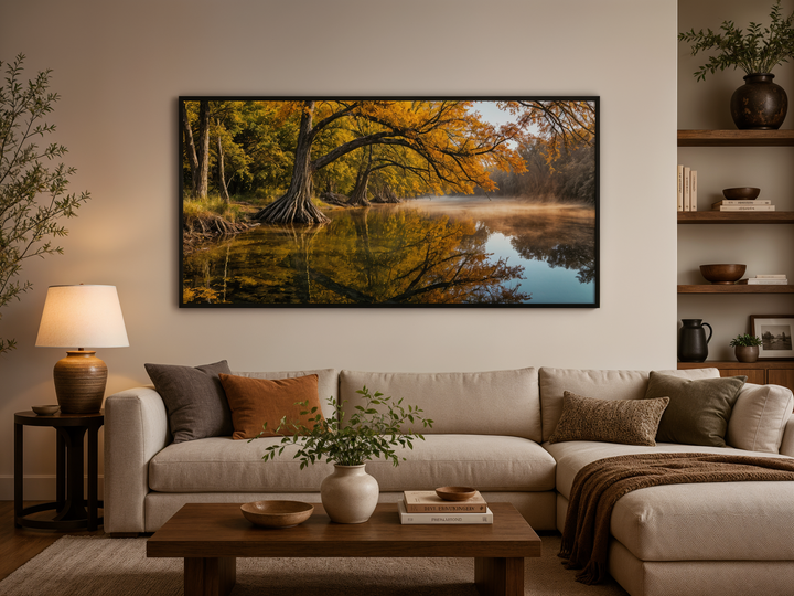 A framed landscape painting of a vibrant fall river scene hangs above a modern neutral sofa.