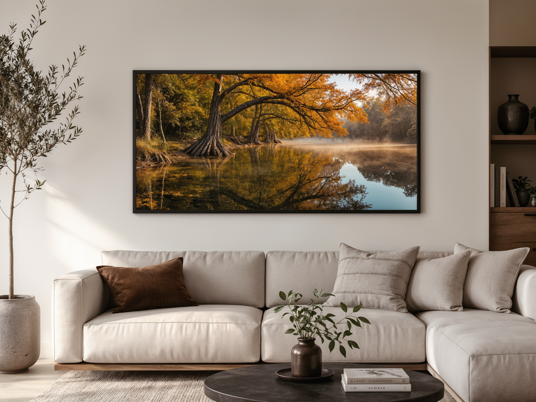 A framed horizontal canvas of a vibrant fall river landscape hangs above a modern neutral sofa.