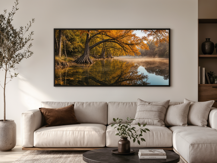 A framed horizontal canvas of a vibrant fall river landscape hangs above a modern neutral sofa.