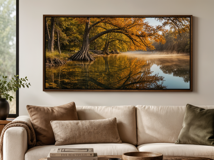 A framed landscape painting of a vibrant fall river scene hangs above a neutral-toned sofa.