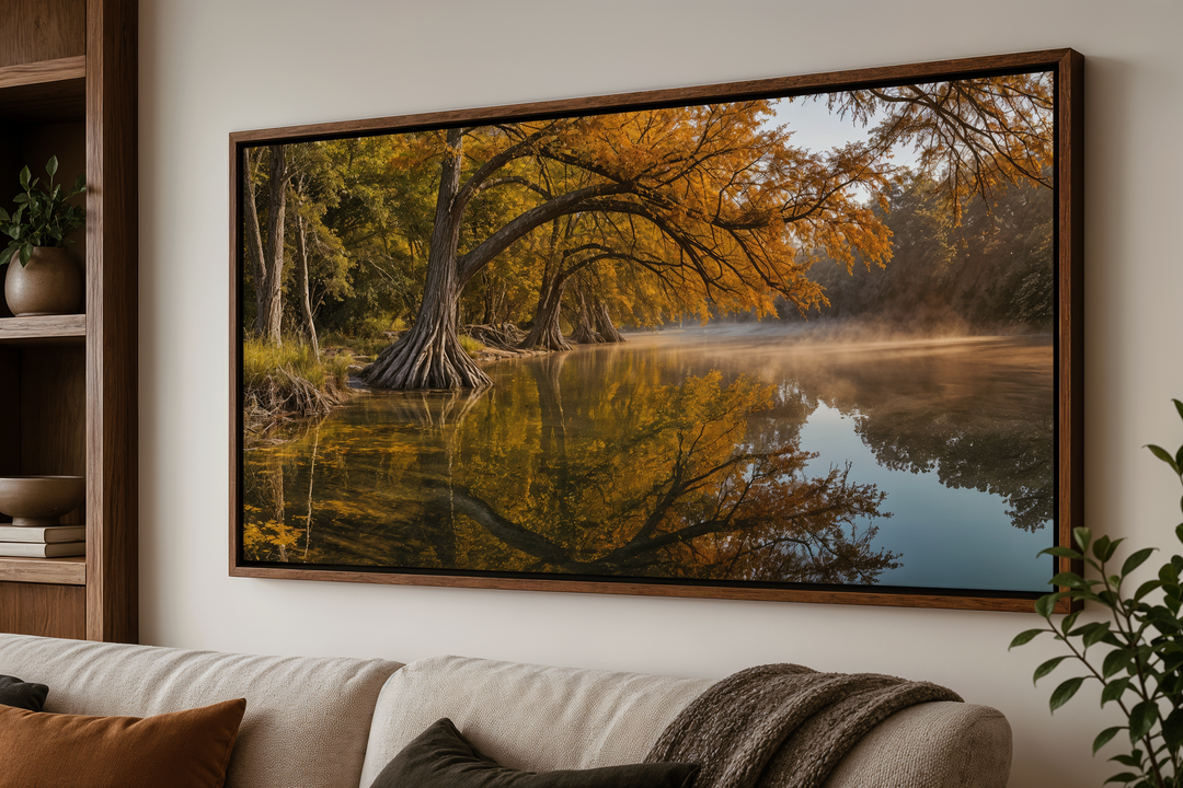 A framed canvas print of a vibrant fall river landscape hangs above a neutral-toned sofa.