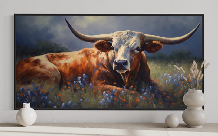 Framed canvas print of a Texas Longhorn cow lying in a field of bluebonnets and wildflowers.