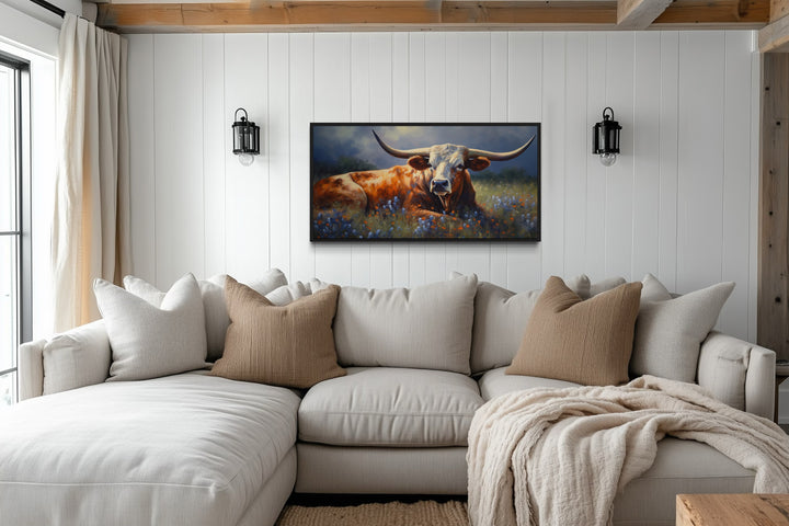 Framed canvas print of a Texas Longhorn in a bluebonnet field above a neutral sectional sofa.