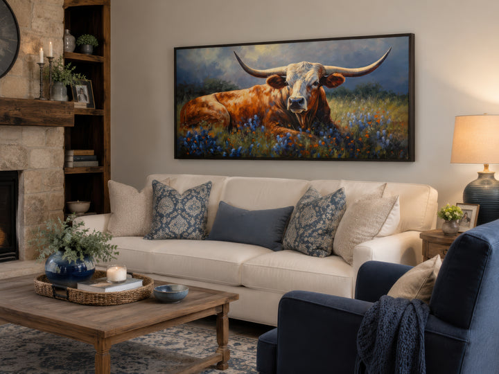 Framed canvas print of a Texas Longhorn cow in a bluebonnet field hanging above a white sofa.