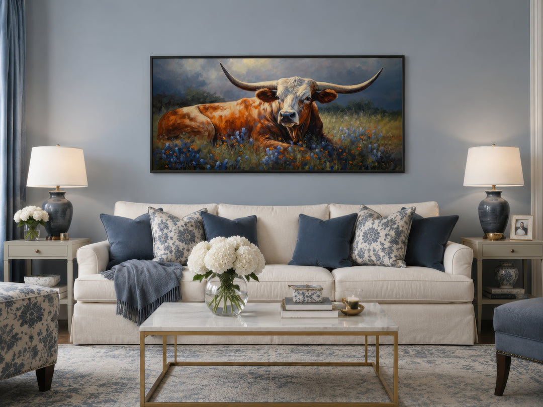 Framed canvas print of a Texas Longhorn cow in a bluebonnet field above a white sofa.