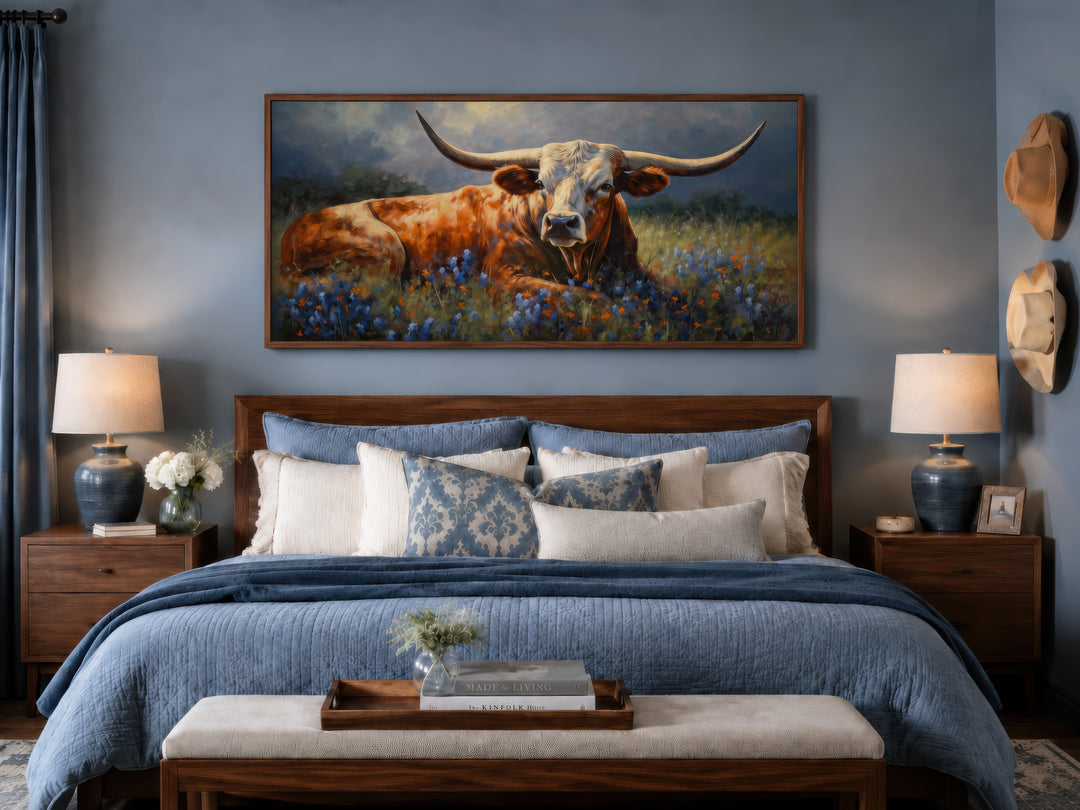 Framed canvas print of a Texas Longhorn cow lying in a bluebonnet field above a bed.
