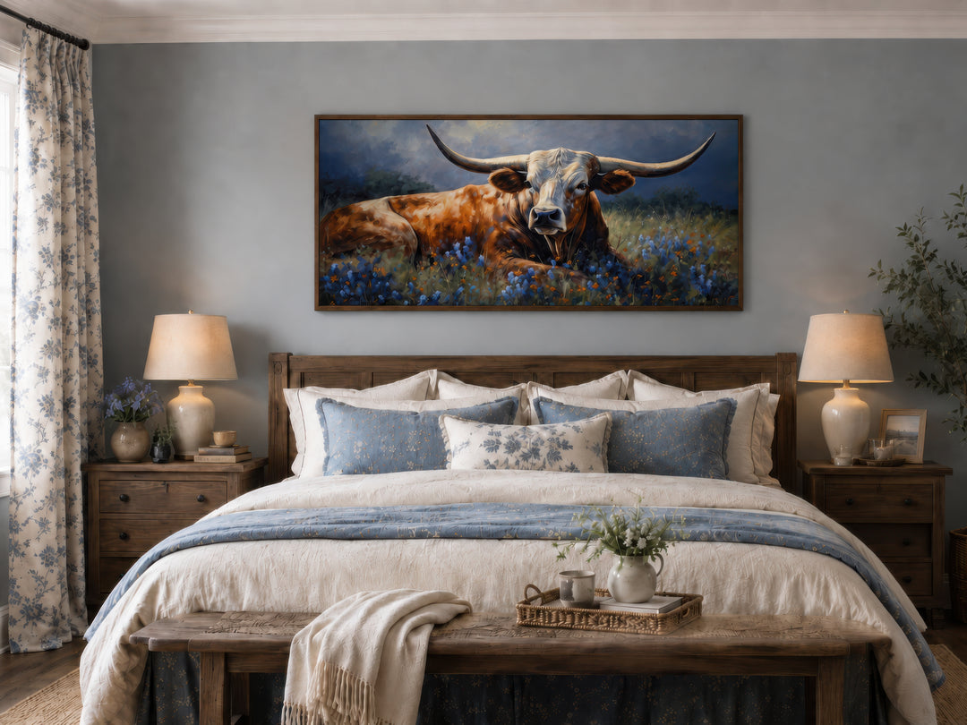 Framed canvas print of a Texas Longhorn cow lying in a bluebonnet field above a farmhouse bed.