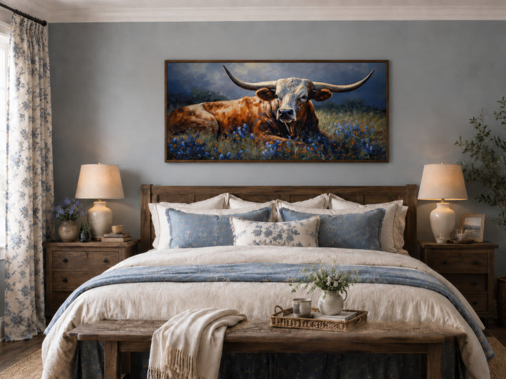 Framed canvas print of a Texas Longhorn cow lying in a bluebonnet field above a farmhouse bed.