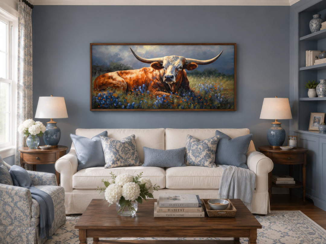 Framed canvas print of a Texas Longhorn cow lying in a field of bluebonnets over a white sofa.