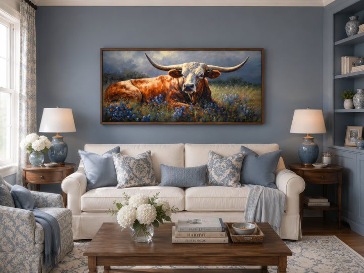 Framed canvas print of a Texas Longhorn cow lying in a field of bluebonnets over a white sofa.