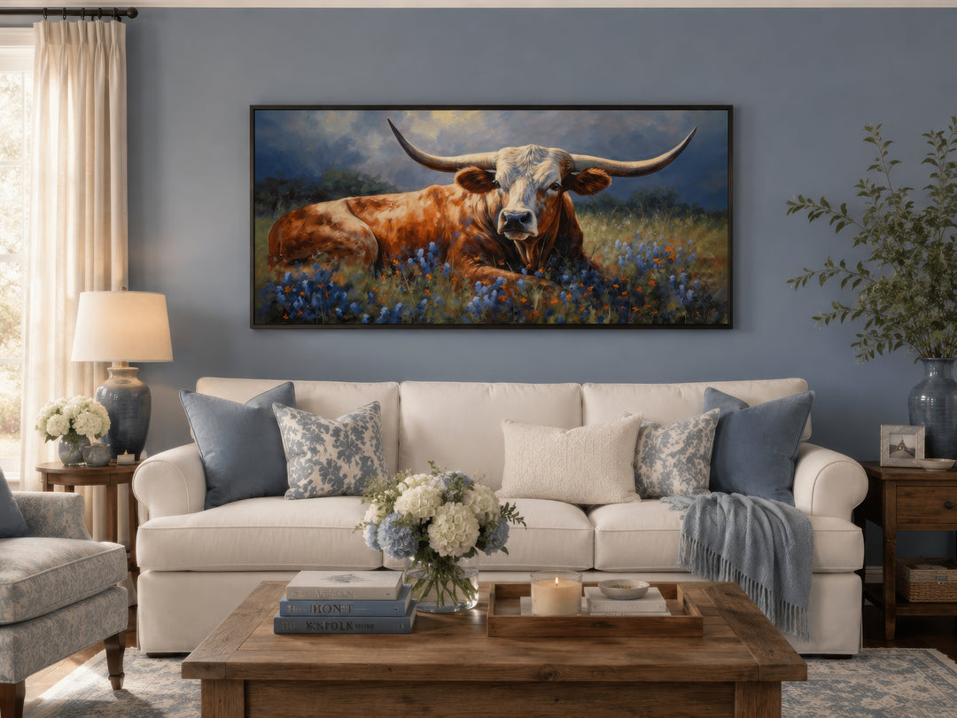 Framed canvas print of a Texas Longhorn in a bluebonnet field above a white sofa in a living room.