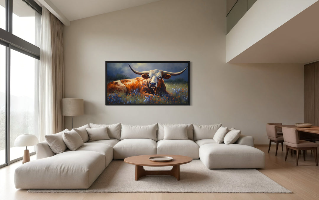 Framed canvas print of a Texas Longhorn cow in a bluebonnet field above a modern sectional sofa.