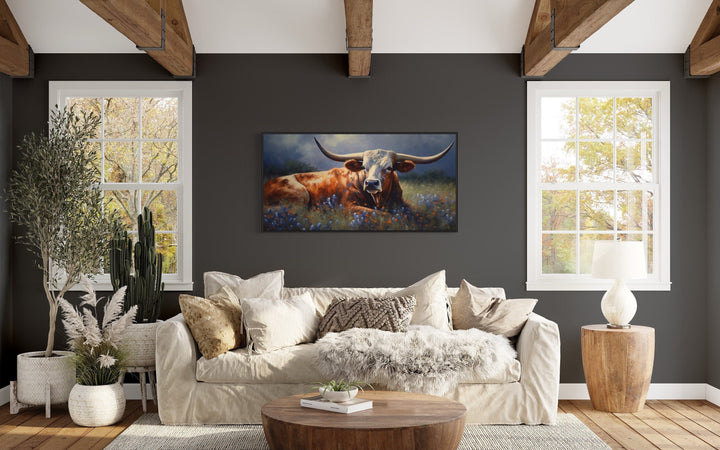 Texas Longhorn cow in a bluebonnet field canvas print framed above a sofa in a rustic living room.