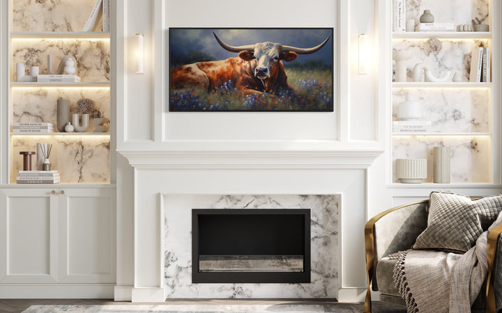 Texas Longhorn cow lying in a bluebonnet field canvas print above a white fireplace mantel.