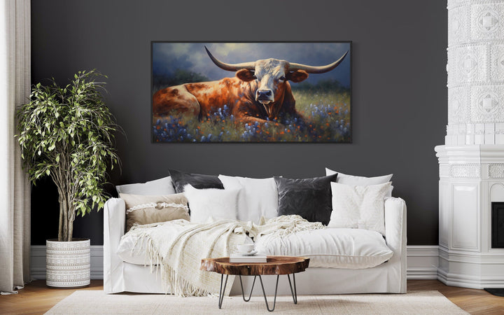 Framed canvas print of a Texas Longhorn cow lying in a bluebonnet field above a white sofa.