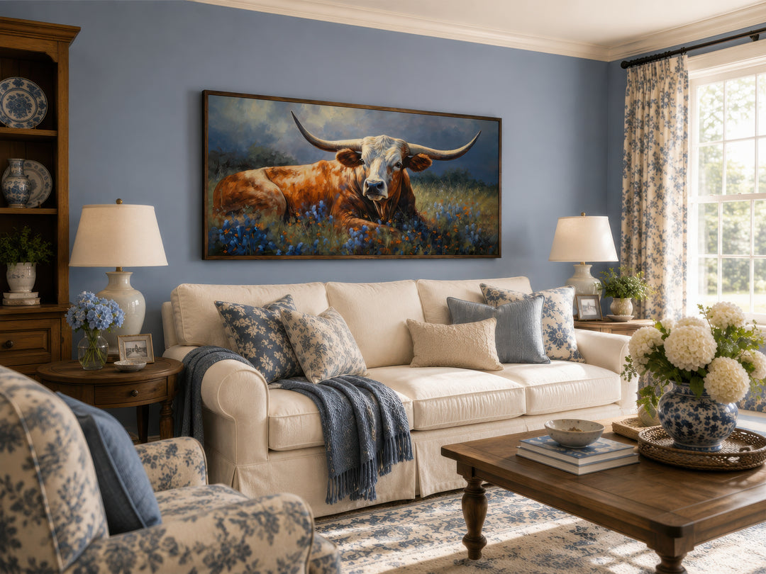 Framed canvas print of a Texas Longhorn in a bluebonnet field above a white sofa in a living room.