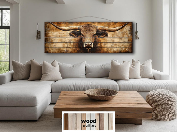 Horizontal wood wall art of a Texas longhorn bull in neutral brown tones above a modern sofa.